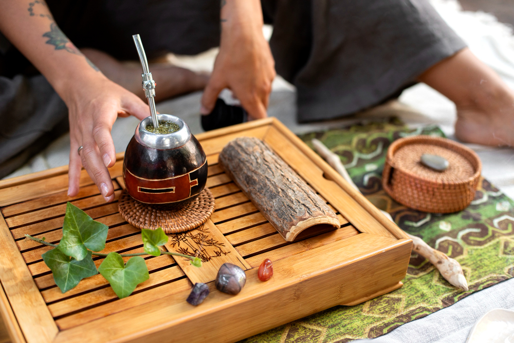 Une personne prépare du maté sur un plateau en bois avec des plantes et cristaux.
