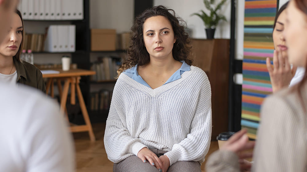 Groupe de personnes en réunion, femme au centre écoutant attentivement.