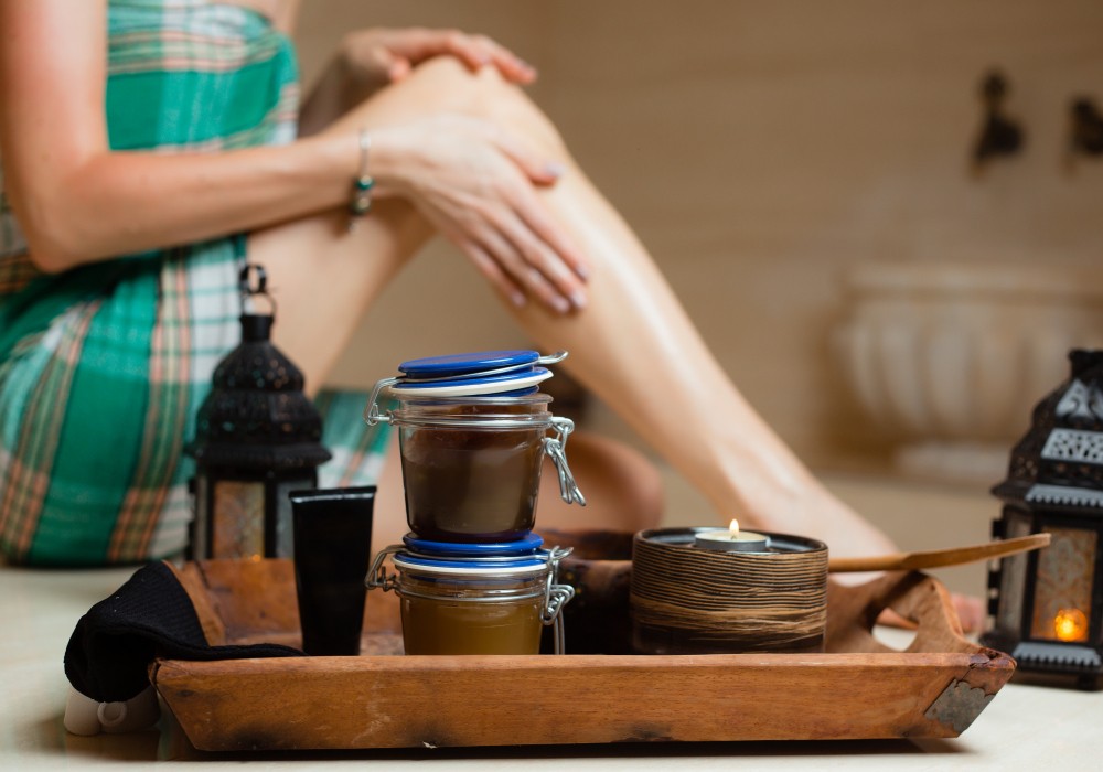 Femme appliquant des soins sur ses jambes avec des produits naturels et bougies.