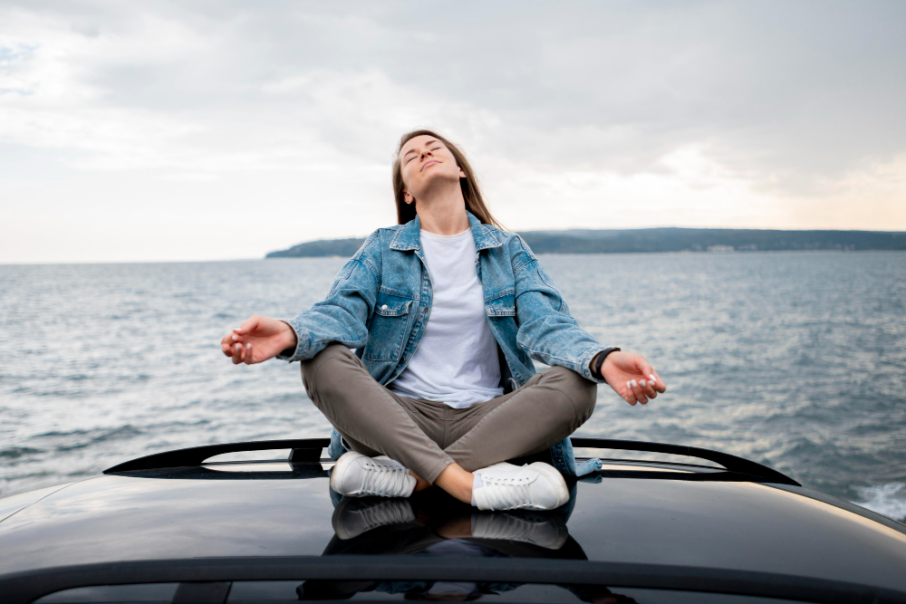 Femme méditant assise sur une voiture près de la mer.