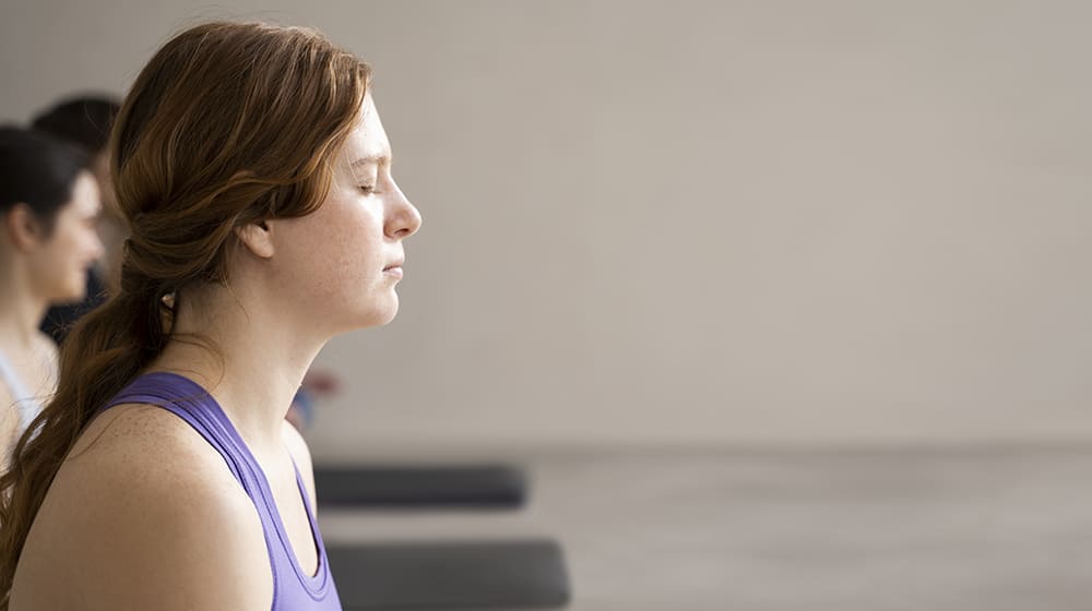 Femme méditant les yeux fermés en classe de yoga.