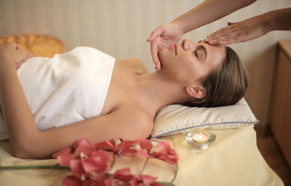 Femme recevant un soin du visage dans un spa, avec bougie et fleurs.
