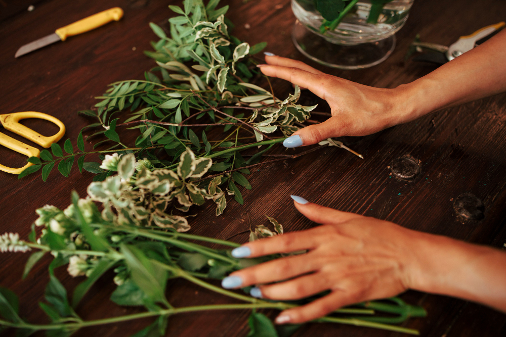 Des mains arrangent des branches et des feuilles sur une table en bois.