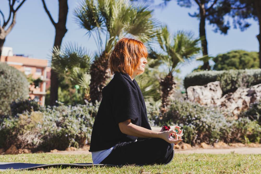 Femme méditant dans un parc en plein air, entourée de végétation.