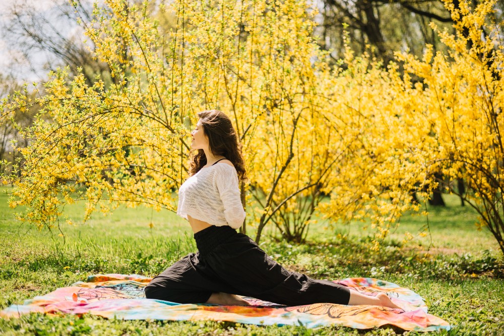 Femme faisant du yoga devant des buissons fleuris jaunes au printemps.