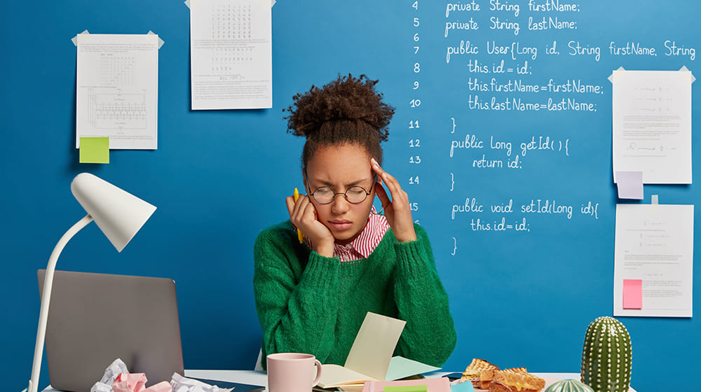 Personne stressée devant un ordinateur avec du code sur un tableau.