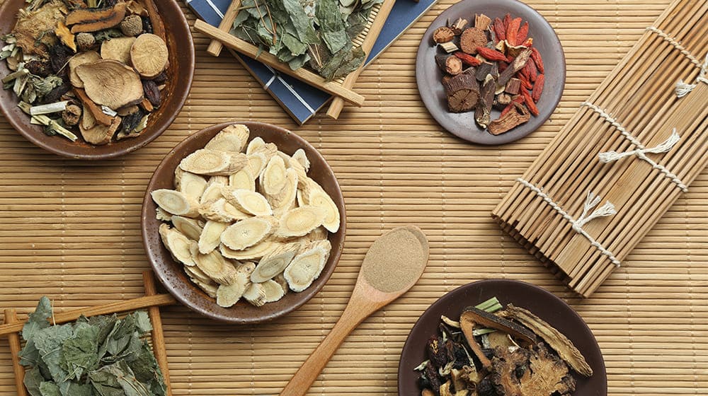 Assortiment d'herbes médicinales séchées sur un tapis en bambou.