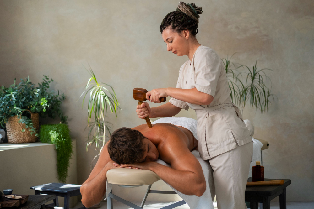 Femme effectuant un massage avec un outil en bois sur un homme allongé.