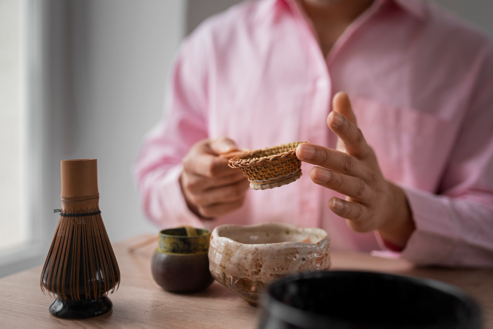 Homme en chemise rose tenant un panier en osier, objets de thé sur la table.