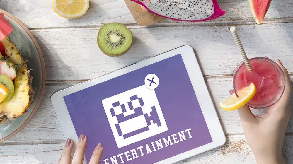 Tablette affichant "Entertainment" avec fruits et boisson sur une table en bois.