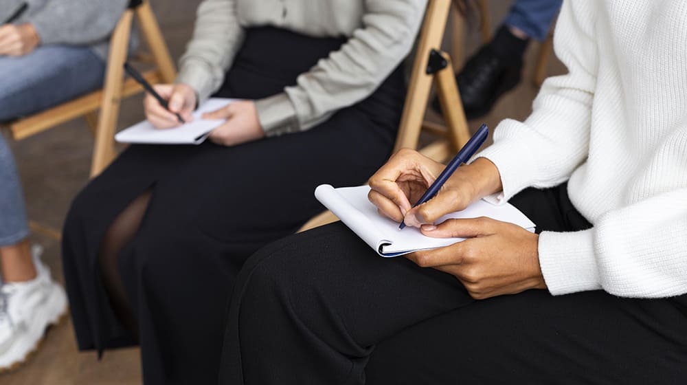 Personnes écrivant dans des carnets lors d'une réunion.