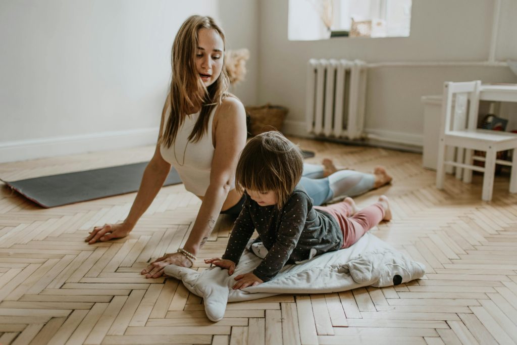 Femme et enfant faisant du yoga ensemble sur le sol en bois.
