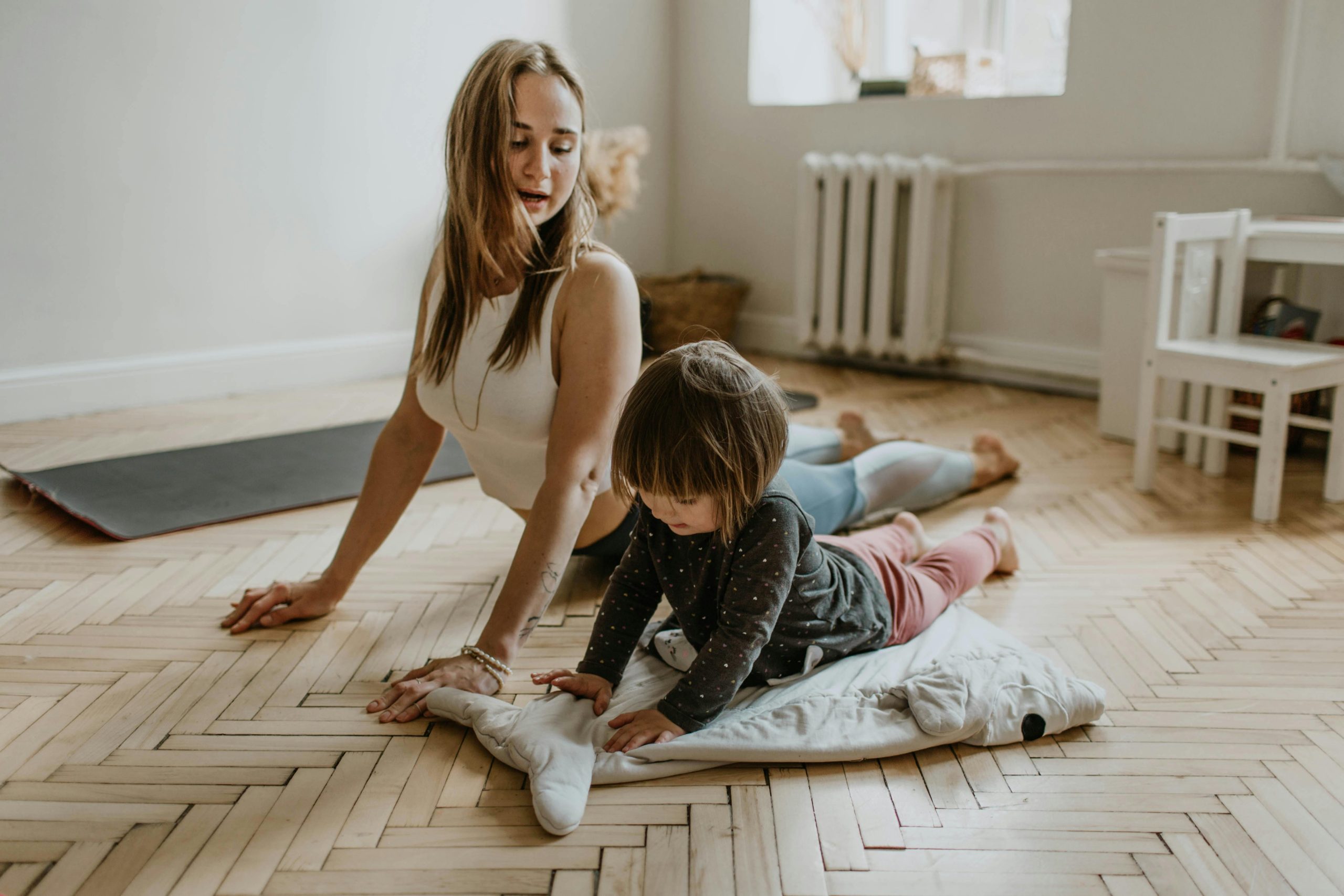 Femme et enfant faisant du yoga ensemble sur le sol en bois.