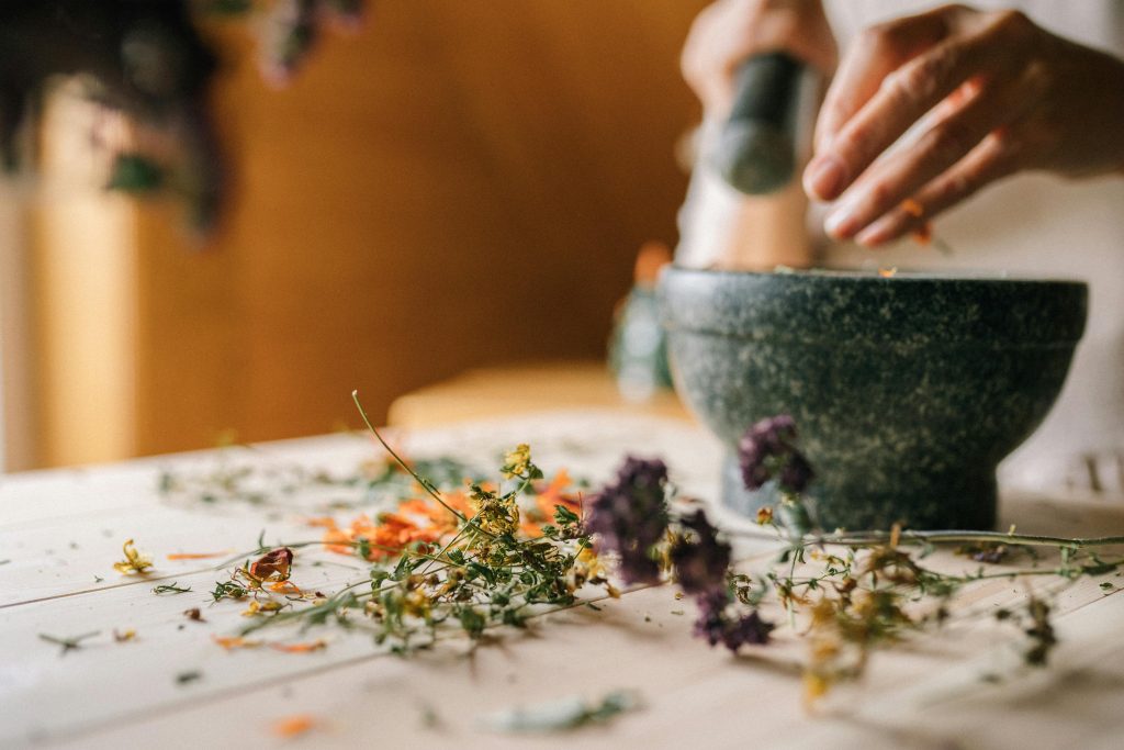 Personne utilisant un mortier et pilon avec des herbes séchées sur la table.
