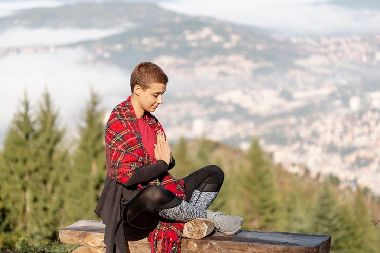 Femme méditant en plein air, assise sur un banc, avec vue sur des montagnes.