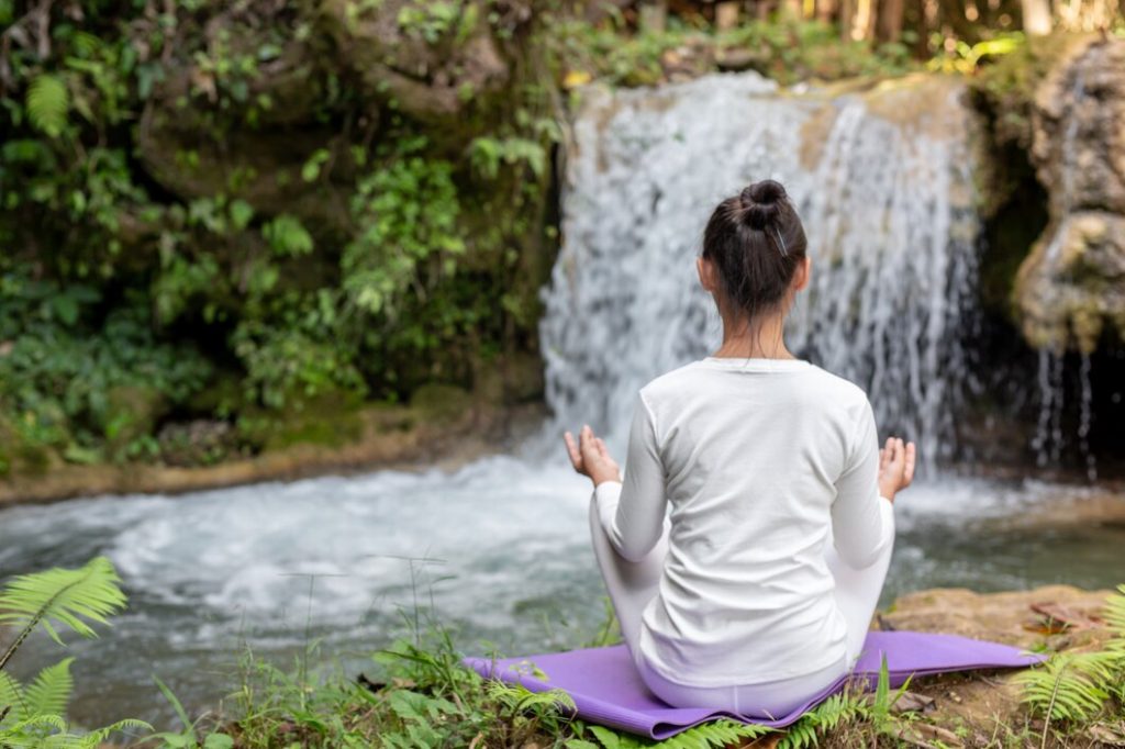 Femme méditant devant une cascade dans la nature.