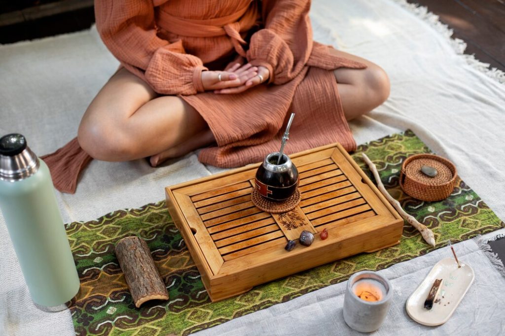 Personne assise en méditation avec accessoires de thé et bougie sur un tapis.
