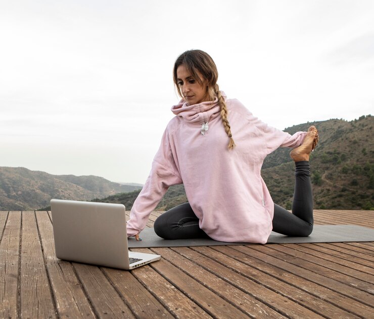 Femme faisant du yoga en plein air devant un ordinateur portable.
